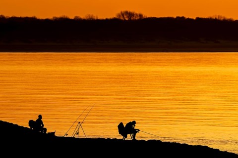 Silhouette of two recreational anglers, fishermen with several fishing rods angling at sunset