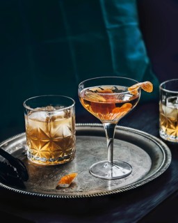A sophisticated whiskey and orange cocktail sits elegantly on an ornate silver tray, accompanied by