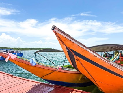 Colorful traditional longtail boats rest alongside a sunlit dock in Phuket, Thailand. The image