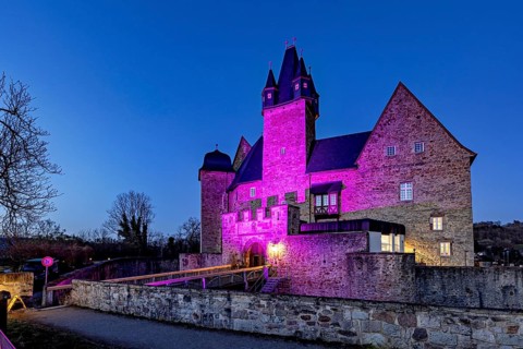 A castle at night, illuminated by pink light with dramatic-looking walls, Spangenberg Castle