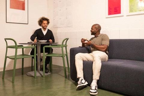 Two men are enjoying a relaxed moment indoors. One man is sipping coffee on a couch, while the