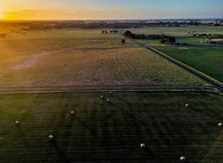 Aerial view of a sprawling countryside landscape with lush green fields and hay bales scattered