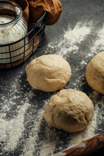 Fresh dough balls rest on a flour dusted black counter top. A glass jar filled with flour is