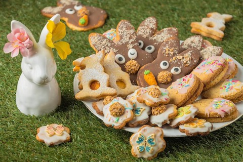 Different Easter cookies on a plate next to a porcelain hare with flowers in the grass
