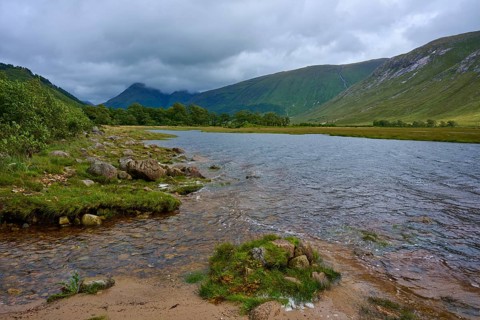 A river flows through a green landscape under a cloudy sky, Loch Etive, Argyll and Bute, Scotland,