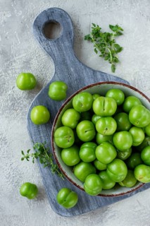 Tkemali, green cherry plum, in a bowl, on a gray table, top view, natural light, no people