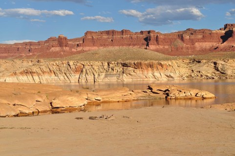 Red rocks tower over a desert-like landscape with calm water under blue skies, Lake Powell,