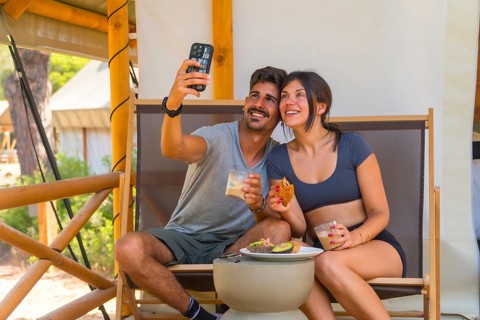 Young couple smiling and taking a selfie with smartphone while having breakfast in a glamping tent,
