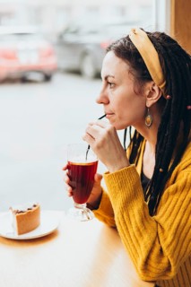 A woman with a yellow headband and warm sweater enjoys a drink through a straw by the window of a