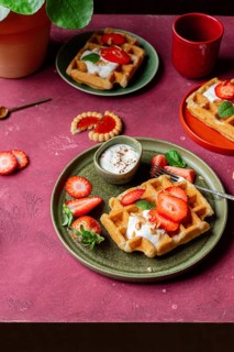 Homemade waffles topped with sweet strawberries and creamy yoghurt on rustic plates. A romantic