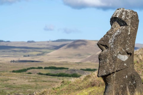 Moai statue in profile on the slope of the Rano Raraku volcano, hilly landscape in the background,
