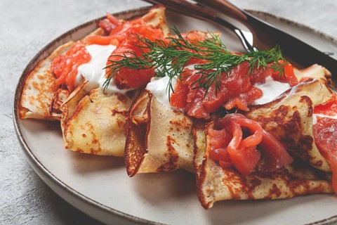 Delicious pancakes with salmon and sour cream, breakfast, on a plate, rustic style, with cutlery
