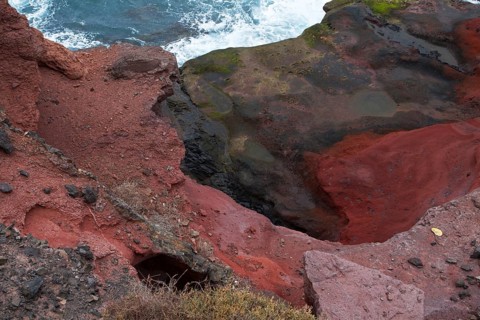 Bizarre red rock formations on the coast with a view of the stormy sea, Playa Blanca