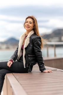 Cheerful woman enjoying a relaxing moment by the sea, wearing a stylish leather jacket and exuding