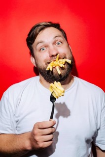 A playful scene featuring fries on a fork and in a man's mouth, against a striking red background.