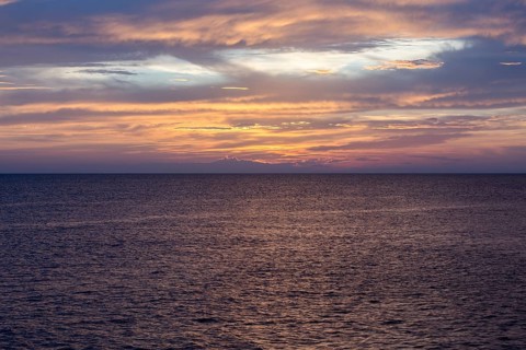 Serene sea scene at sunset with vibrant orange, pink, and purple hues reflecting on the water. The