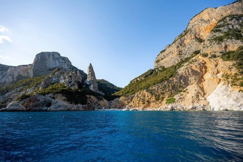 Picturesque rocky coast, cliffs with caves in the morning light, L'Aguglia rock peak, blue sea and