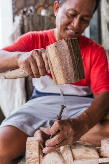 An Indonesian man skillfully carves a wooden sculpture using traditional tools, highlighting ethnic