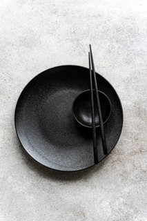 Minimalist black table setting featuring a sleek plate and bowl with chopsticks on a textured gray