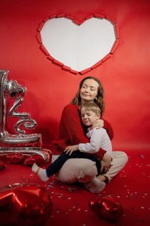 A mother and her young son embrace warmly amidst Valentine's decorations, including heart-shaped