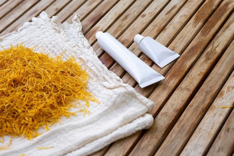 Marigold petals on a cloth beside white cosmetic tubes of marigold petals cream on a wooden surface
