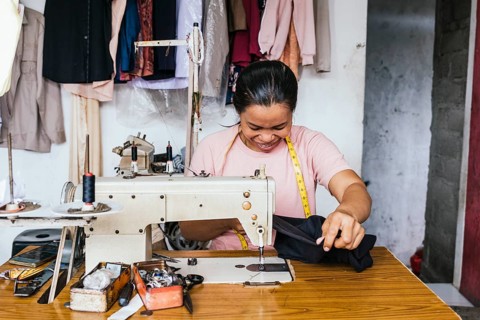 A asian seamstress diligently works with a sewing machine, surrounded by tools and fabrics in a