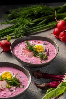 A vibrant bowl of cold beetroot soup garnished with fresh herbs, radish slices, and a boiled egg.