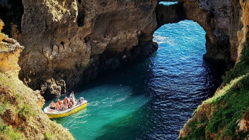 Small boat with tourists in turquoise water in front of an impressive rock formation, rock arch and