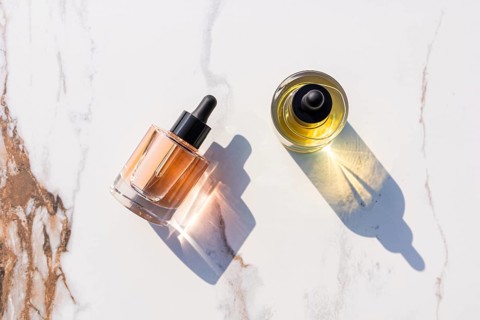 Two skincare dropper bottles on a marble surface, casting soft shadows. The golden hued liquids