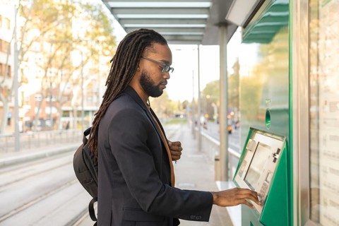 A cuban business man with glasses and a backpack uses a ticket machine at a tram stop in an urban