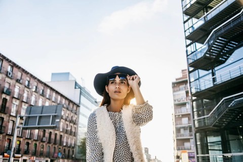 Stylish woman in a city street wearing a black hat, sunglasses, and a leopard-pattern top. Urban