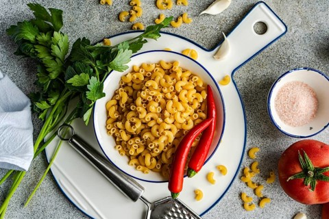 A bowl of uncooked chifferi rigati pasta is artfully displayed with fresh parsley, red chili