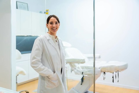 Smiling female doctor in a white coat stands in a modern aesthetic clinic, confident and