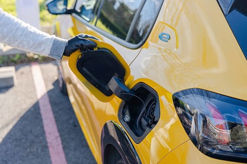 A person in gloves plugs a yellow electric car into a charging station. The scene highlights