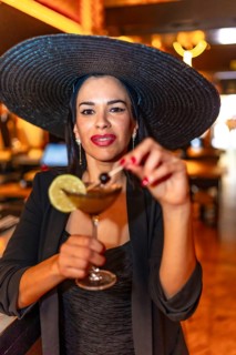 Vertical close-up portrait of an elegant caucasian adult woman with black dress and hat drinking a