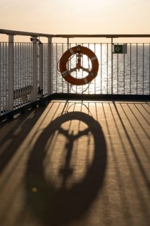 The lifebuoy on the railing casts long shadows at sunset on the upper deck of the TT-Line Nils