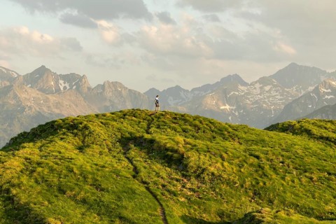 A man pauses on a grassy trail, capturing a moment of serenity with stunning mountainous views in