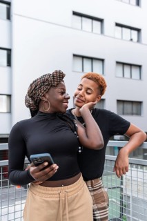 A joyful LGBT multiethnic couple shares a tender moment outdoors, leaning against a railing with