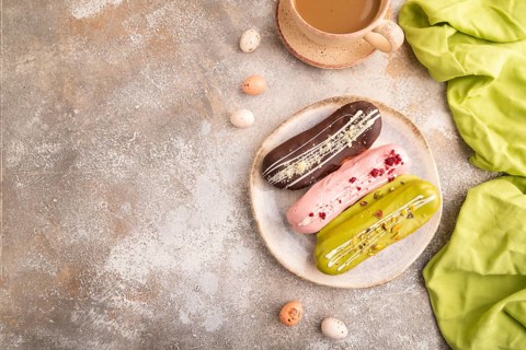 Glazed Eclairs on brown concrete background and green linen textile, cup of coffee, top view, flat