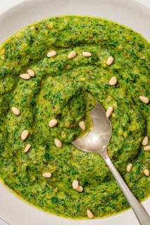 Top view of a rich, vibrant green pesto sauce, dotted with pine nuts and red pepper flakes, served