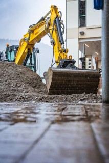 A yellow excavator doing earthworks next to a building on a wet road, Hermann Hesse railway