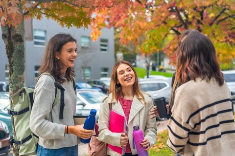 Diverse group of young women students laughing and chatting on a university campus in autumn,