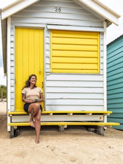 A woman enjoys a sunny day while sitting at the vibrant Brighton Bathing Boxes. These iconic