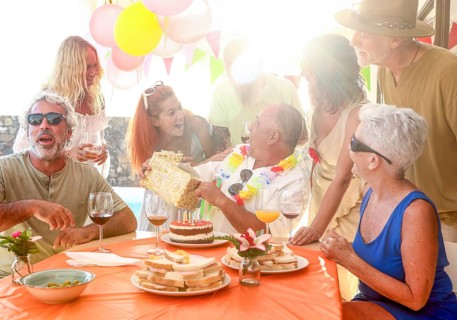 A lively group of friends gathers outdoors to celebrate a birthday. Laughter, gifts, and joy are