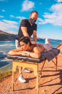 A young man performing a massage in nature on the coast near the sea, masseuse with a face mask in