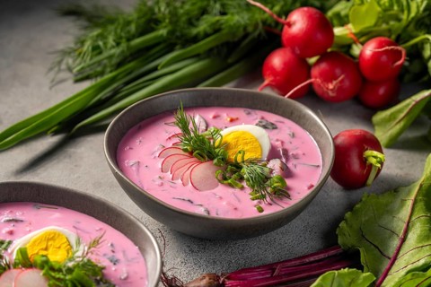 A bowl of chilled beetroot soup garnished with a slice of hard-boiled egg, fresh dill, and radish