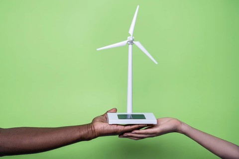 Close-up of diverse hands holding a small wind turbine model against a vibrant green background,