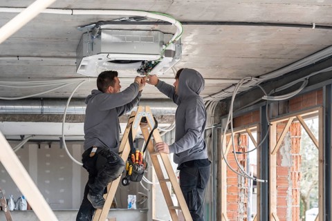 Hvac technicians working on a ladder, connecting wires to an air conditioning system mounted on the