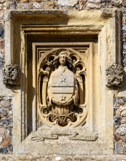 Carved stonework architectural detail exterior of figure holding heraldic shield, church of Saint