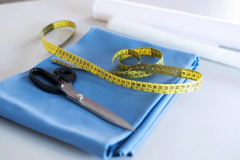 A folded piece of blue fabric with a yellow measuring tape and tailorâ€™s scissors placed on top,